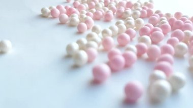 Small mother-of-pearl white and pink balls or make-up powder beads roll on a white background, minimal idea concept, 4k video