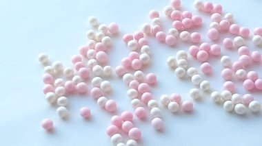 Small mother-of-pearl white and pink balls or make-up powder beads roll on a white background, minimal idea concept, 4k video