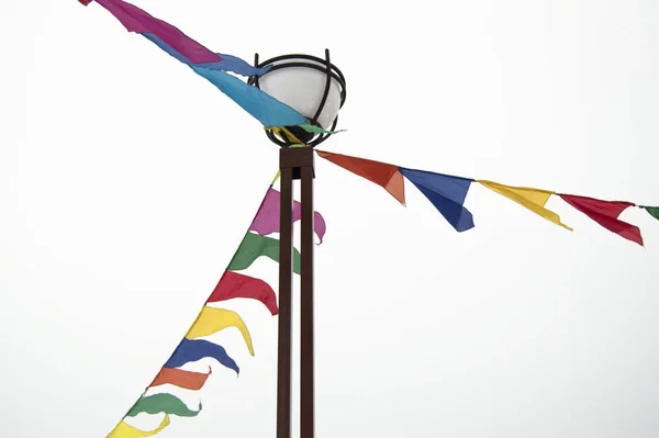 Ünnepi háromszög alakú zászlók füzérek lógnak egy lámpaoszlopra kötve. Dekorációs ötletek ünneplésére egy esemény, elszigetelt fehér alapon — Stock Fotó