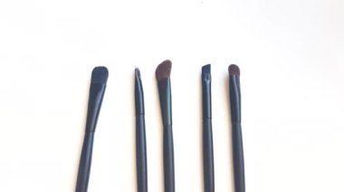 Set of black makeup brushes and cosmetics on a white background, beauty concept. Slow motion, top view, 4k video, clean unused brushes.