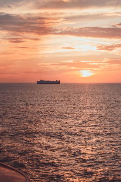 Um lindo pôr-do-sol rosa e dourado no mar, um navio no horizonte, nuvens românticas no céu, um tiro vertical — Fotografia de Stock