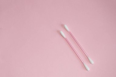 Üst manzara, düz yatak, iki pembe plastik pamuklu çubuk. Pembe arka plan, temizlik ve hijyen kavramı..