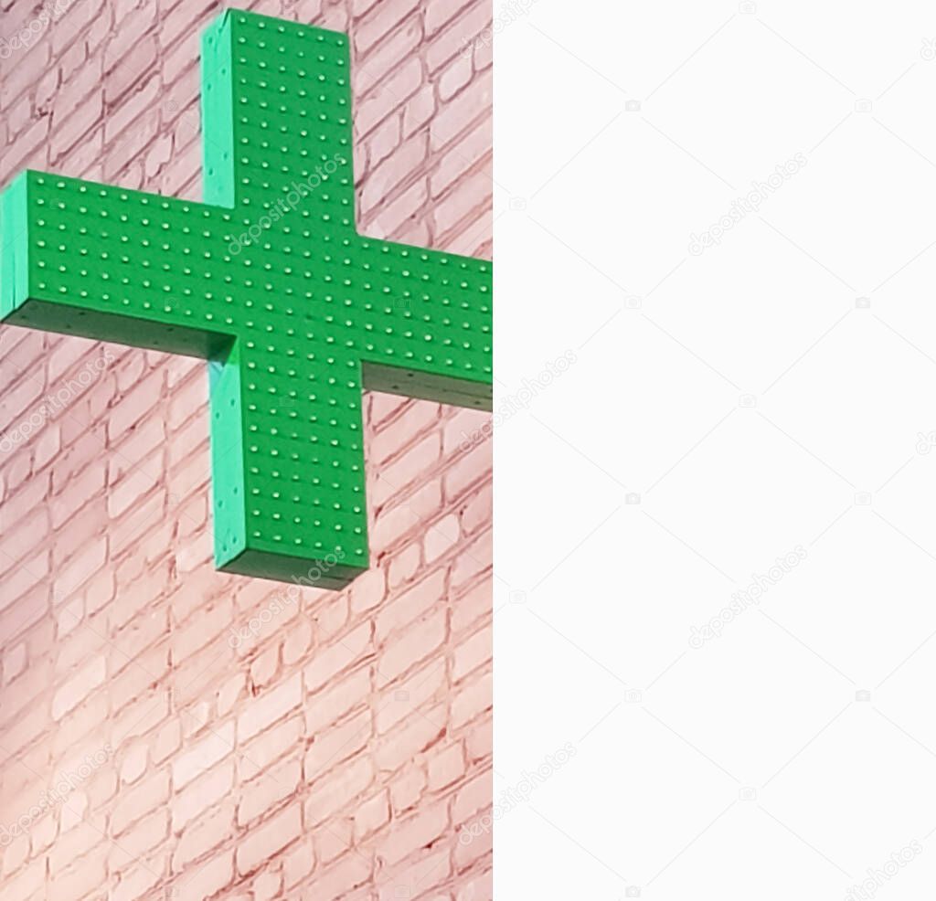 Green cross neon sign of a pharmacy on the street against a brick wall, concept of medical care and treatment, copy of the space.