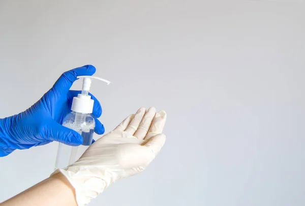 A pair of hands in blue and white rubber gloves hold a white bottle with sanitary spray on a gray background, a copy of the text space. Spring cleaning in a commercial cleaning company.