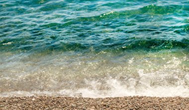 Güneşli bir yaz gününde turkuvaz suyu ve çakıl taşı plajı olan deniz kıyısının yakın görüntüsü, sakin deniz, seyahat ve tatil konsepti..