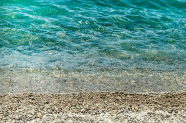 Güneşli bir yaz gününde turkuvaz suyu ve çakıl taşı plajı olan deniz kıyısının yakın görüntüsü, sakin deniz, seyahat ve tatil konsepti..