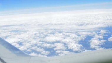 Uçağın kanadında, uçağın penceresinden bulutların üzerinde uçarken, parlak güneş gökyüzünde parlarken. Hava yoluyla seyahat eden bir uçak. HD video