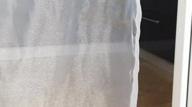4K video. Şeffaf ışık perdeleri rüzgarda sallanıyor, balkona açılan açık bir kapı, odanın manzarası...