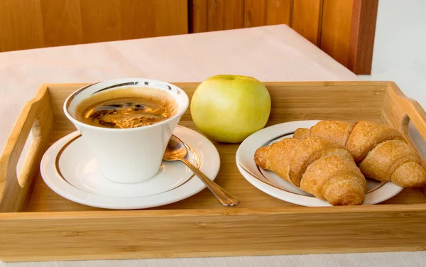 Desayuno continental tradicional con café expreso, cruasanes y una manzana en una bandeja de madera — Foto de Stock