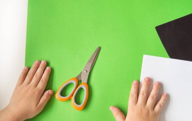 DIY ve çocukların yaratıcılığı kavramı. Adım adım talimatlar: Kağıttan Panda uygulaması nasıl yapılır. Birinci adım. Renkli kağıt ve makas hazırlayın. Çocuğun elleri masanın üstünde..