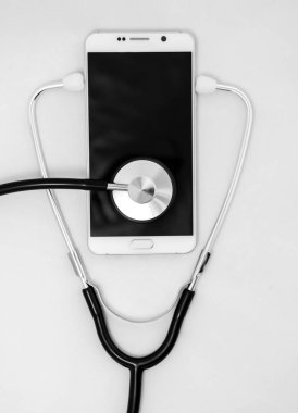 Mobil bir akıllı telefon, beyaz arka plan üzerinde izole kompozisyon yüzey üzerinde sağlık stetoskop aracı. Seçici odak ile