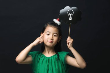 şirin Asyalı kız çocuk Noel kafa dekorasyonu ile sopa bir fikir ampul siyah bir arka plan üzerinde tutarak yeşil renkli bir elbise giymiş. Bir düşünce ifade