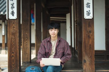 Güney Kore'de seyahat genç adam. Kore geleneksel evde oturan bir dizüstü bilgisayar kullanarak.