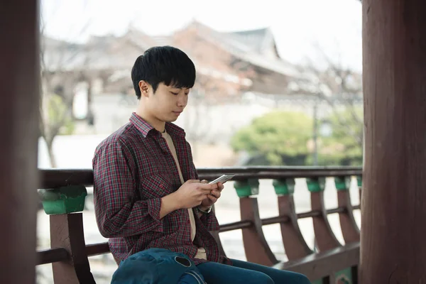一个年轻男子在韩国传统的房子里做背包旅行 使用智能手机 — 图库照片