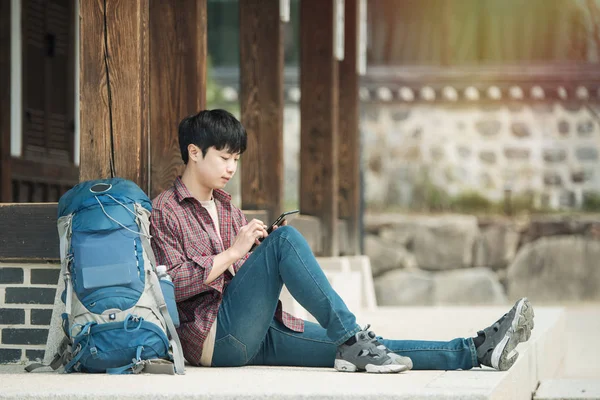 韓国でバックパックを背負って若い男 韓国の伝統的な家に座っていると タブレット コンピューターを使用して — ストック写真