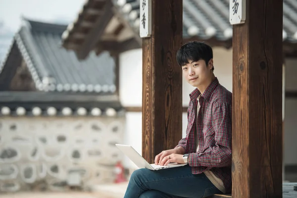 韓国旅行の若い男 韓国の伝統的な住宅に座ってラップトップを使用してください — ストック写真