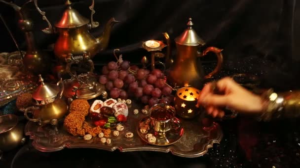 Женщина с восточными украшениями пьет чай и ест традиционные марокканские сладости. Чашка чая с сафроном и масалой — стоковое видео