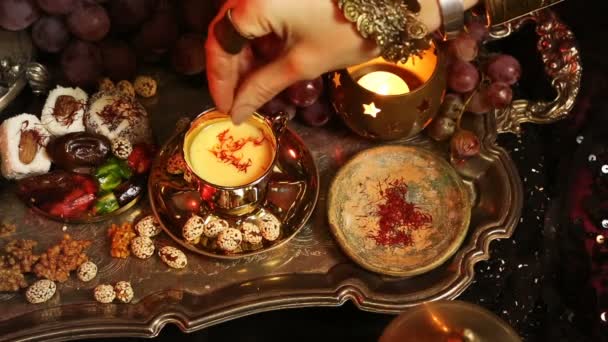 Mãos femininas com jóias orientais Fazendo Chá em Copo. Doces marroquinos tradicionais. Xícara de chá de leite Saffron Masala — Vídeo de Stock