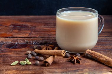 Baharatlı Masala çayı geleneksel bir Hint içkisidir. İçindeki malzemelerin yanında koyu arkaplanda masala çayı olan bir bardak. Tarçın, kakule, anason. Boşluğu kopyala. 