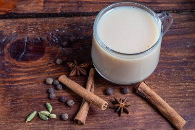 Baharatlı Masala çayı geleneksel bir Hint içkisidir. İçindeki malzemelerin yanında koyu arkaplanda masala çayı olan bir bardak. Tarçın, kakule, anason. Boşluğu kopyala. 