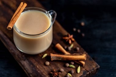 Baharatlı Masala çayı geleneksel bir Hint içkisidir. İçindeki malzemelerin yanında koyu arkaplanda masala çayı olan bir bardak. Tarçın, kakule, anason. Boşluğu kopyala. 