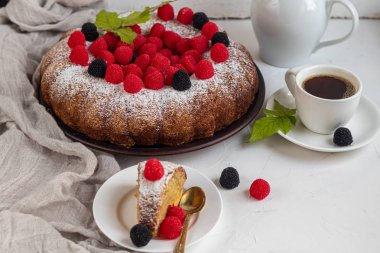 Noel, üzerine pudra şekeri serpiştirilmiş tatil pastası. Ahududu ve böğürtlenli. Yakınlarda bir fincan sıcak kahve var. Beyaz arka planda. Boşluğu kopyala. 