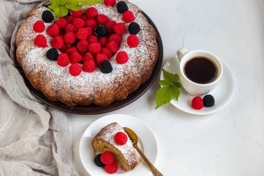 Noel, üzerine pudra şekeri serpiştirilmiş tatil pastası. Ahududu ve böğürtlenli. Yakınlarda bir fincan sıcak kahve var. Beyaz arka planda. Boşluğu kopyala. 