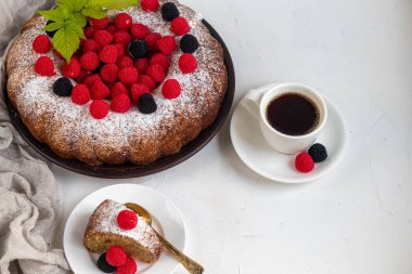 Noel, üzerine pudra şekeri serpiştirilmiş tatil pastası. Ahududu ve böğürtlenli. Yakınlarda bir fincan sıcak kahve var. Beyaz arka planda. Boşluğu kopyala. 