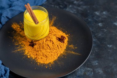 Bardakta sütlü sütlü sağlıklı zerdeçal içeceği. Safranlı altın süt, zencefil kökü, tarçın çubuğu ve koyu arkaplanda bal. Detoks çayı. Sağlıklı yeme alanı kopyala. 