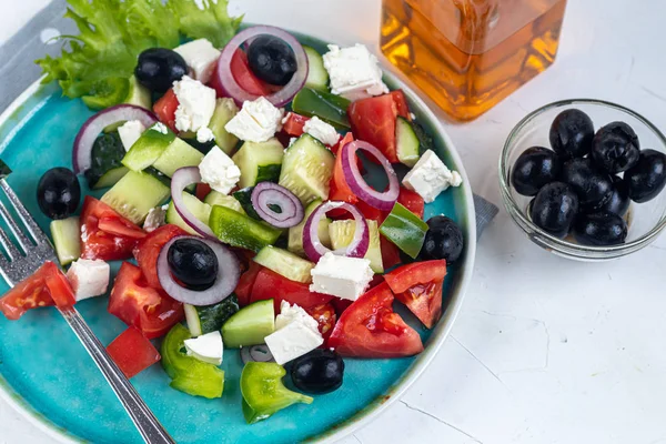 Greek salad. Diced tomatoes, cucumbers, feta cheese, olives. Rings of red onion. Food for vegetarians. Festive and New Year\'s dish. On a light background. Copy space.