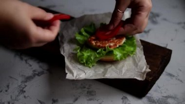 Evde hamburger pişiriyorum. Aşamalı yerleşim. Tavuk pirzolası, soğan, sebze, krem peynir ve marullu büyük aperatif burger..