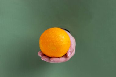 Kadın eli bir portakal tutuyor. Bir kağıt parçasıyla deliğe sokulmuş. Sağlıklı yeme alanı kopyala