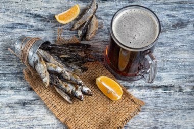 Küçük, tuzlu balık ve bir bardak koyu bira. Limon dilimlerinin yanında. Bir ışıkta, ahşap arka planda.