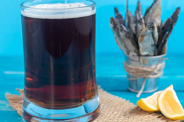 Liten, saltad fisk med ett glas mörk öl. Uppfattat utrymme. Bakgrund tonad i klassisk modern blå 2020. — Stockfoto