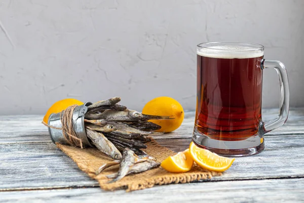Petit poisson salé avec un verre de bière noire. Près des tranches de citron. Sur un fond clair et en bois . — Photo