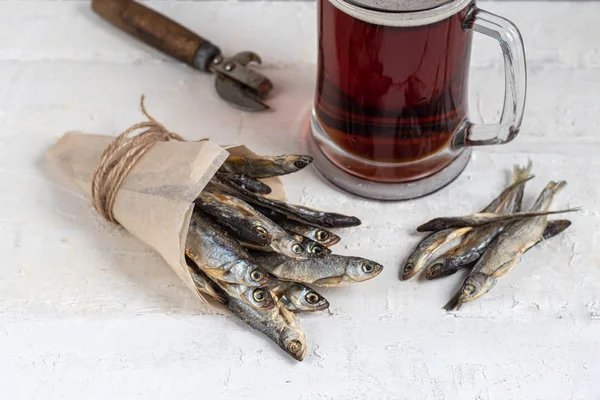 Small, salted fish with a glass of dark beer. Near the slices of lemon. On a light, wooden background.