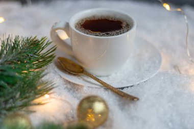 Sıcak kahveyle birlikte beyaz fincan. Yapay karın üzerinde duruyor. Ladin dalının yanında. Yeni Yıl ve Noel.