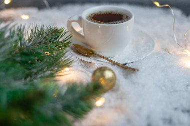 Sıcak kahveyle birlikte beyaz fincan. Yapay karın üzerinde duruyor. Ladin dalının yanında. Yeni Yıl ve Noel.