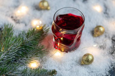 Şenlikli bir içecekle şeffaf cam. Sıcak şarap ya da komposto. Yapay karda duruyor..
