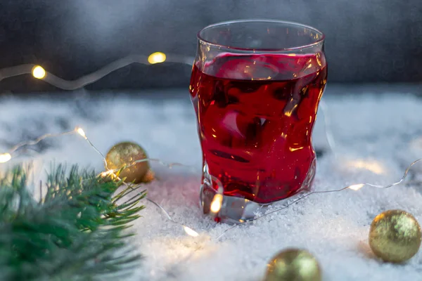 Transparentes Glas mit einem festlichen Getränk. Glühwein oder Kompott. steht im Kunstschnee. — Stockfoto