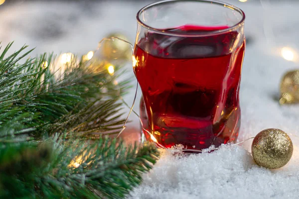 Transparentes Glas mit einem festlichen Getränk. Glühwein oder Kompott. steht im Kunstschnee. — Stockfoto