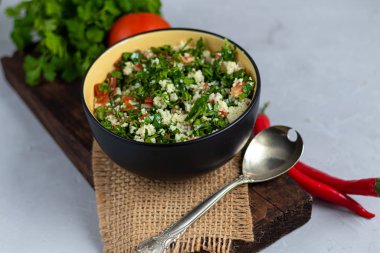 Tabbouleh salatası yuvarlak bir tabakta açık gri arka planda betonun altında.