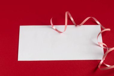 Sevgililer Günü konsepti. Kırmızı bir arkaplanda, ortada yazı için beyaz bir dikdörtgen var. Kalpler ve kurdeleler.