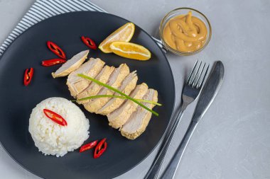 Fırında haşlanmış beyaz pirinçli tavuk göğsü. Kırmızı biber, yeşil soğan şeritleri ve limon dilimleriyle süslenmiş..