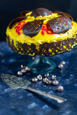 Sarı tereyağlı krema sürülmüş ve çikolata figürleriyle süslenmiş sünger kek. Mavi bir masa örtüsü ve mavi bir arkaplan üzerinde