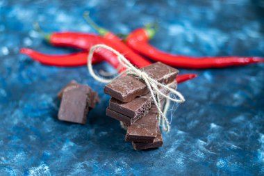 Masada fındıklı siyah gözenekli çikolata, yakın plan. Koyu mavi arka plan 2020. Arka planda kırmızı biber var..