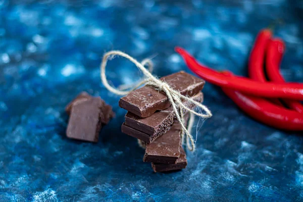 Chocolate poroso oscuro con nueces en la mesa, primer plano. Fondo de tendencia azul oscuro 2020. En el fondo está el chile rojo . — Foto de Stock