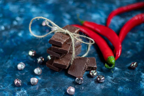 Chocolate poroso oscuro con nueces en la mesa, primer plano. Fondo de tendencia azul oscuro 2020. En el fondo está el chile rojo . — Foto de Stock