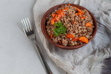 Haşlanmış havuçlu karabuğday lapası. Yeşil yapraklarla süslenmiş. Pamuk peçeteye, açık gri üzerine .