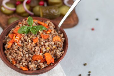 Haşlanmış havuçlu karabuğday lapası. Yeşil yapraklarla süslenmiş. Pamuk peçeteye, açık gri üzerine .